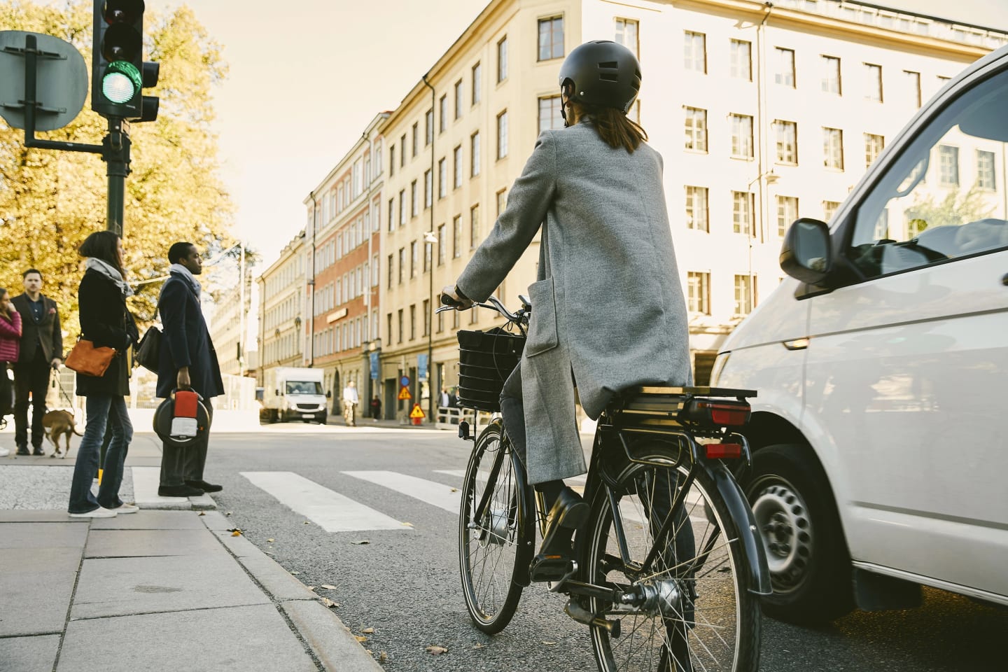 En cyklist står vid ett övergångsställe och bredvid kör en vit bil.