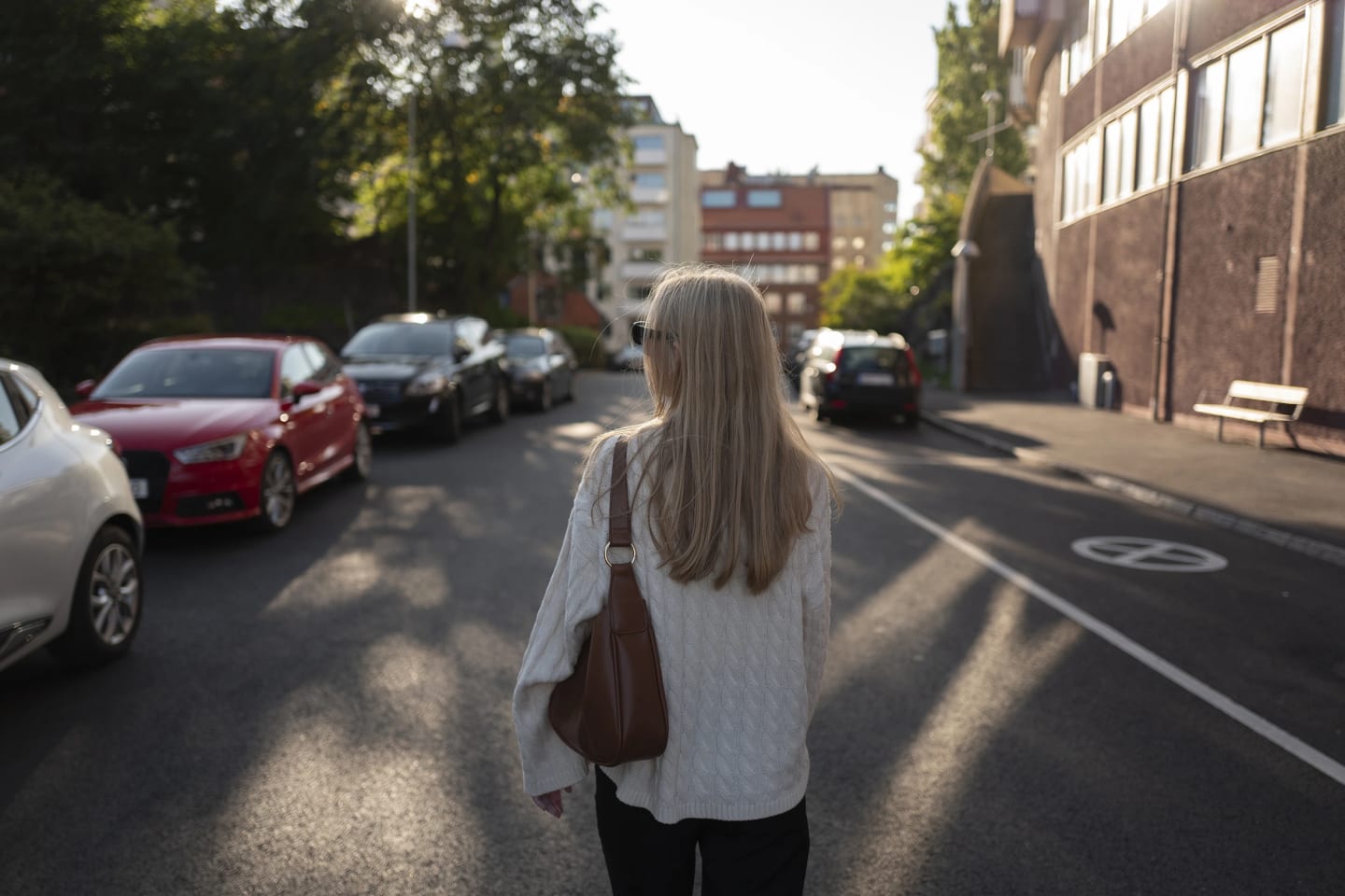 Bild tagen bakifrån på kvinna som går längst gatan i lugn och ro. Längst gatan står flera bilar parkerade.