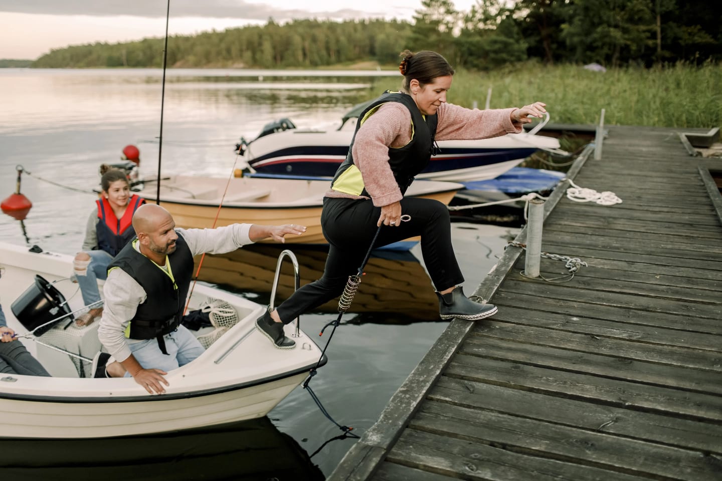 Familj i en båt som ska lägga till vid en brygga. Mamman är i färd att kliva upp på bryggan.