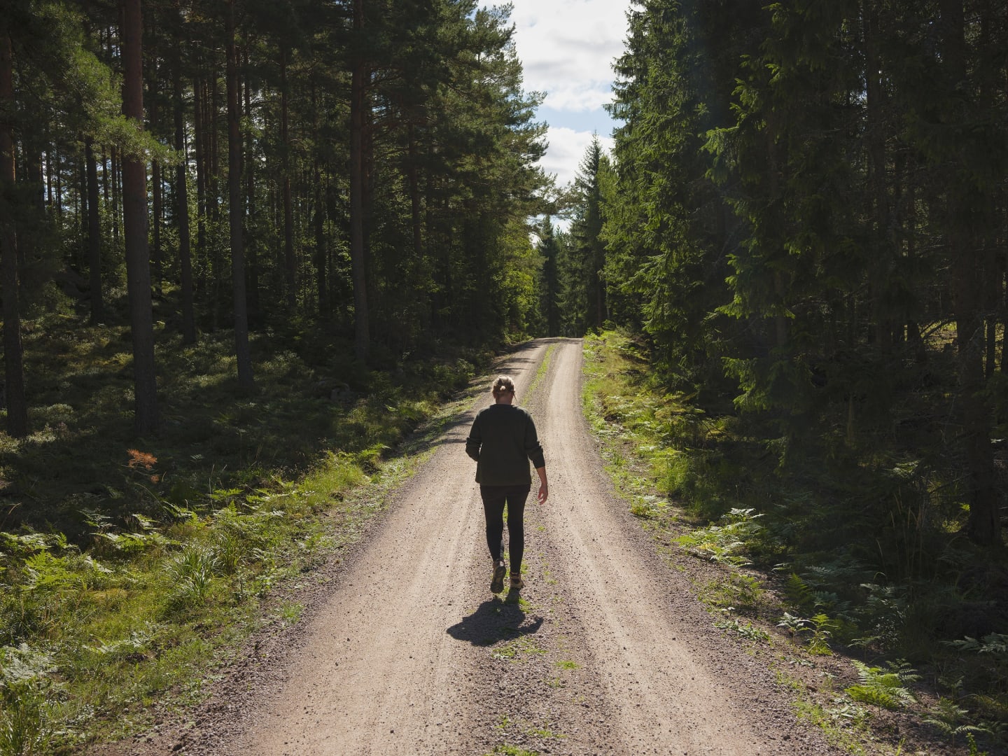 En kvinna syns bakifrån när hon går på en grusväg som är omgiven av skog.