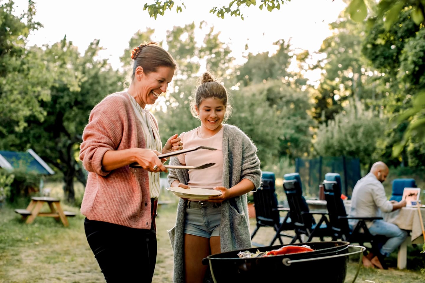 En mamma och dotter står utomhus och grillar och ser glada ut.