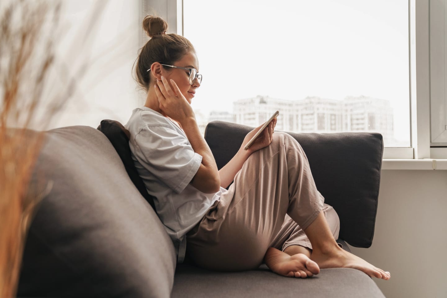 En kvinna sitter i soffan med ett lugnt ansiktsuttryk och tittar på telefonen.
