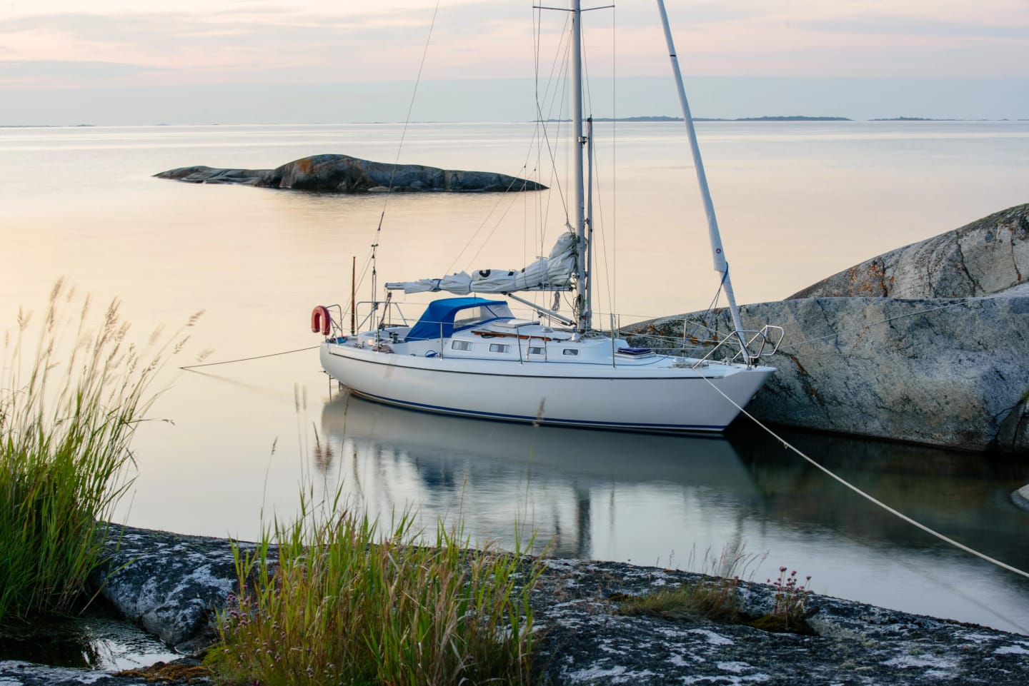 En segelbåt ligger förtöjd intill klippa i skärgården.