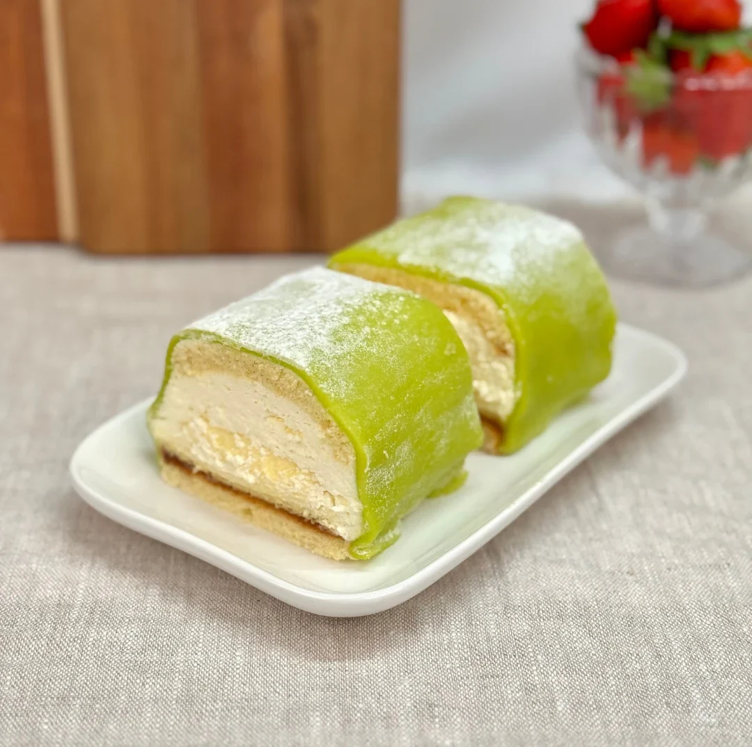 Två bitar prinsessbakelse täckta med grön marsipan och florsocker, serverade på ett vitt fat.