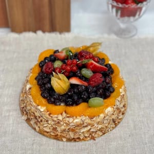Frukttårta med grädde, täckt med mandelspån på sidorna och toppad med blåbär, hallon, jordgubbar, röda vinbär, physalis, vindruvor och mandarinklyftor.