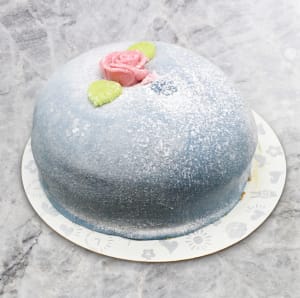 En klassisk kupolformad prinsesstårta täckt med ljusblå marsipan, pudrad med florsocker och dekorerad med en rosa marsipanros.