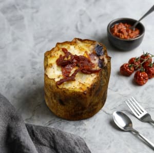 potatisbakelse toppad med krämig fyllning, en bit soltorkad tomat, en oliv och en kvist färsk basilika.