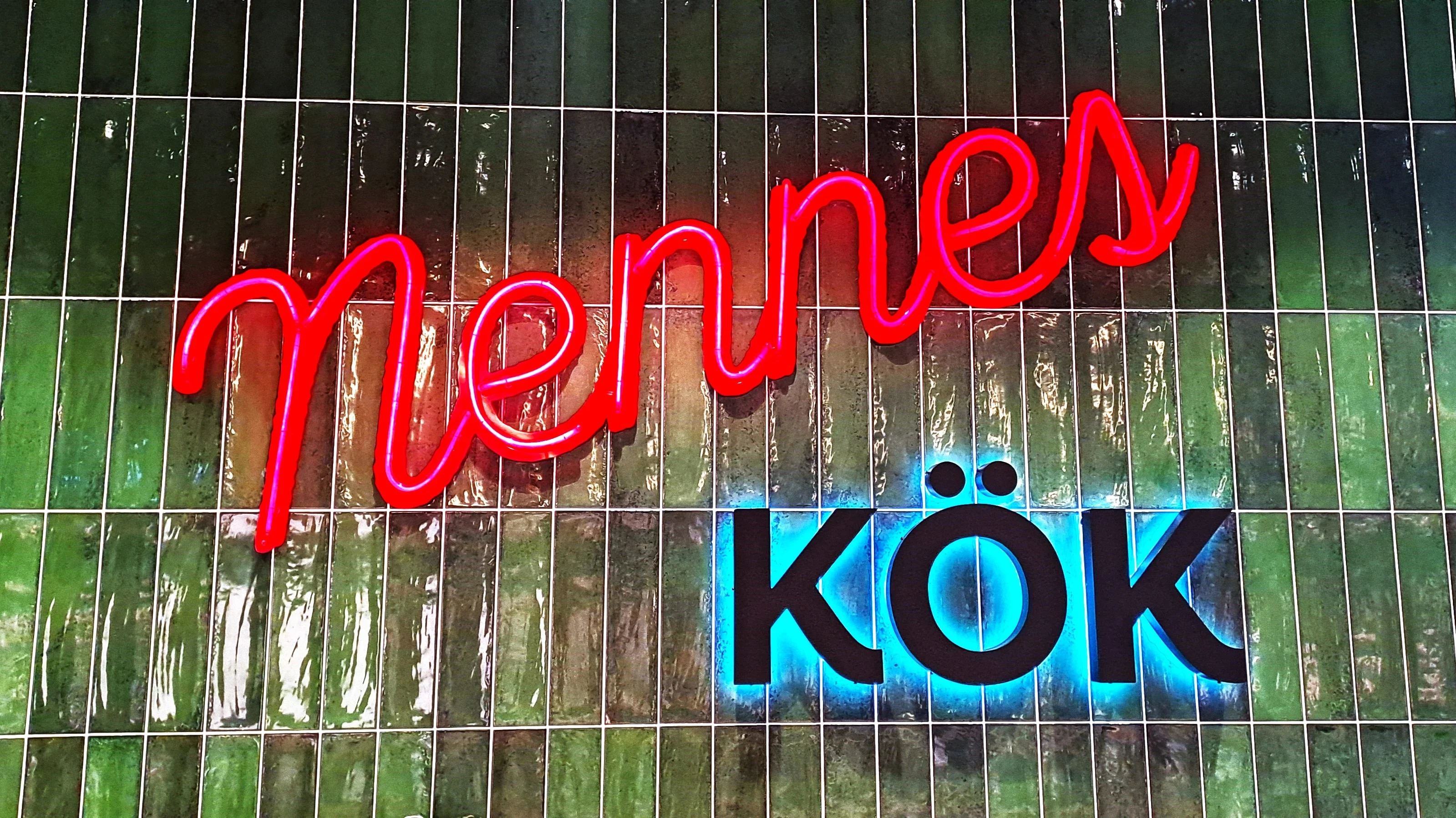 Grön kakelvägg med neonskylt "Nennes kök"