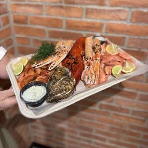En skaldjursplatå med ostron för 2 personer som innehåller 1 hummer, havskräftor, rökta- och färska räkor, ostron, baguette från vårt bageri, aioli och limeaioli, citron, lime och dill.