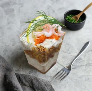 En krämig skagencocktail i glas, rikligt toppad med handskalade räkor, röd stenbitsrom, en citronskiva och en kvist färsk dill.