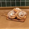 fem stycken kanelbullar i rosa bullpapper på en träbricka framför grönt kakel
