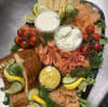 En lax och skaldjursbricka som bjuder på färska räkor, kallrökt lax, gravad lax, pepparlax, skaldjurspaté, romsås, limeaioli, hovmästarsås och toppad med grönsaker.