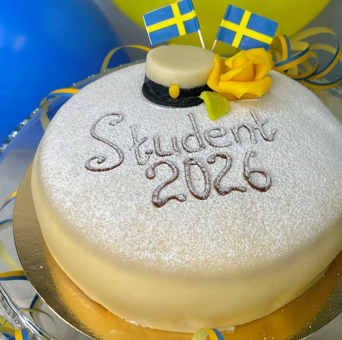 Tårtan är fylld med vaniljkräm och vispgrädde. Dekorerad med en vacker studentmösse, Sverigeflaggor, marsipanros och blad.