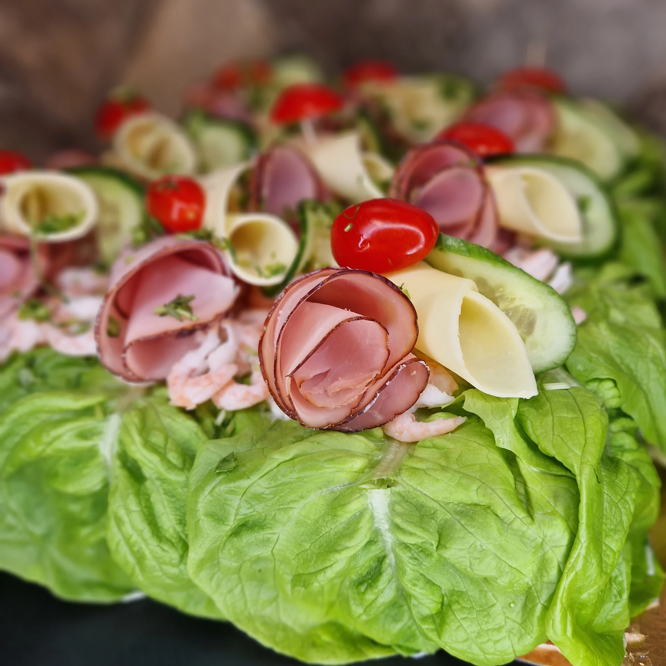 Närbild på smörgåstårta med skinka och handskalade räkor. ost och skinkrullar samt krispig sallad, tomat, gurka