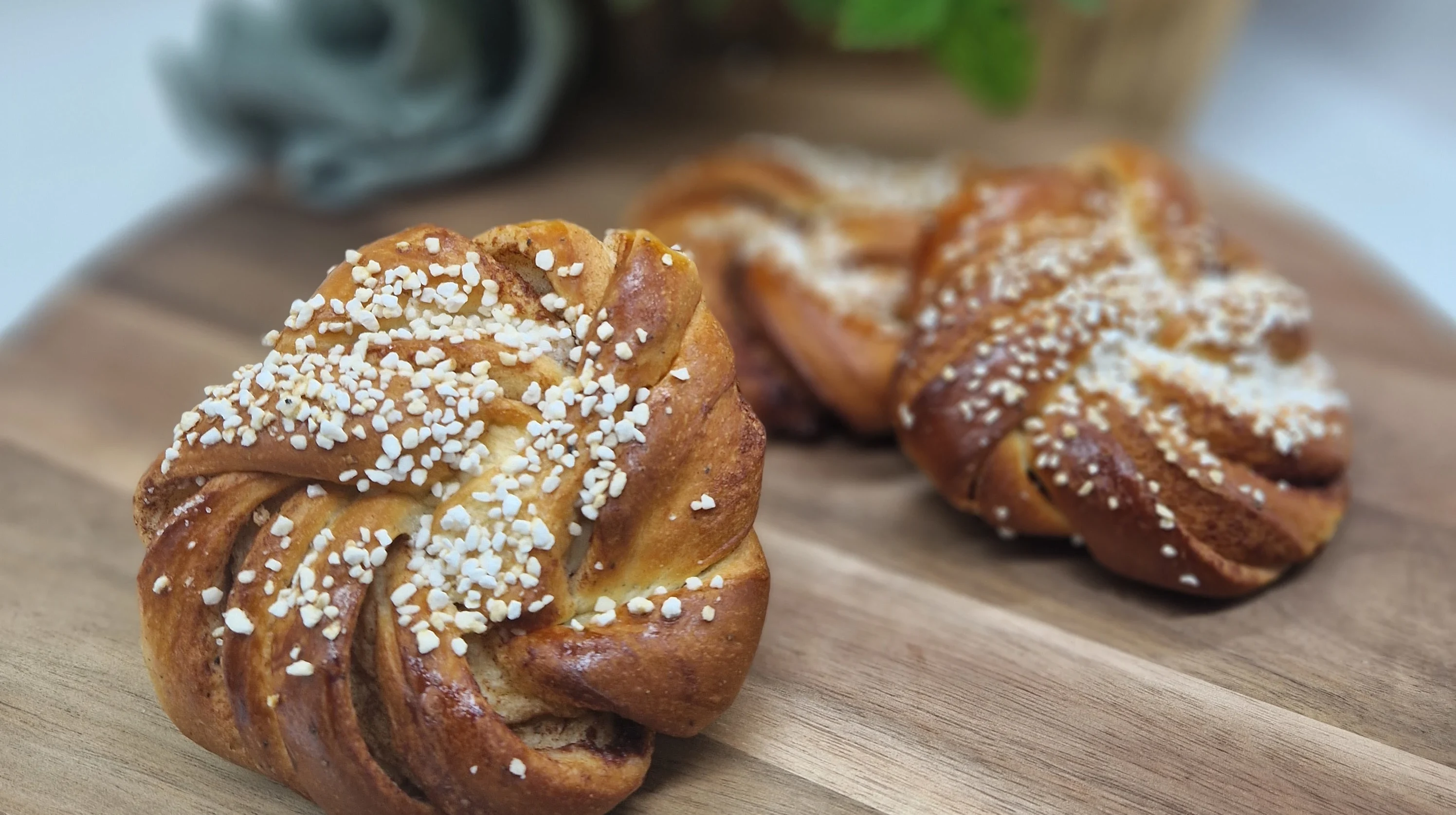Tre stycken kanelbullar, upplagda på träbricka. dekorerade med pärlsocker