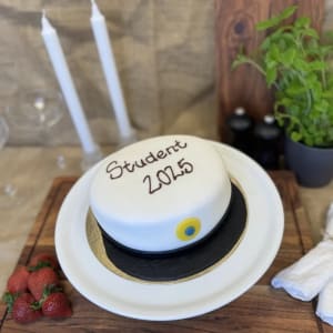 Klassisk studentårta! Saftiga sockerkaksbottnar varvas med fyllning av hallonsylt, kokt vaniljkräm och lättvispad grädde. Överdragen med marsipan formad som en studentmössa.