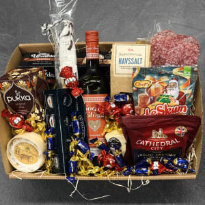 En stor julkorg fylld med julprodukter, såsom julte, glögg, ostar, salami, skumtomtar.