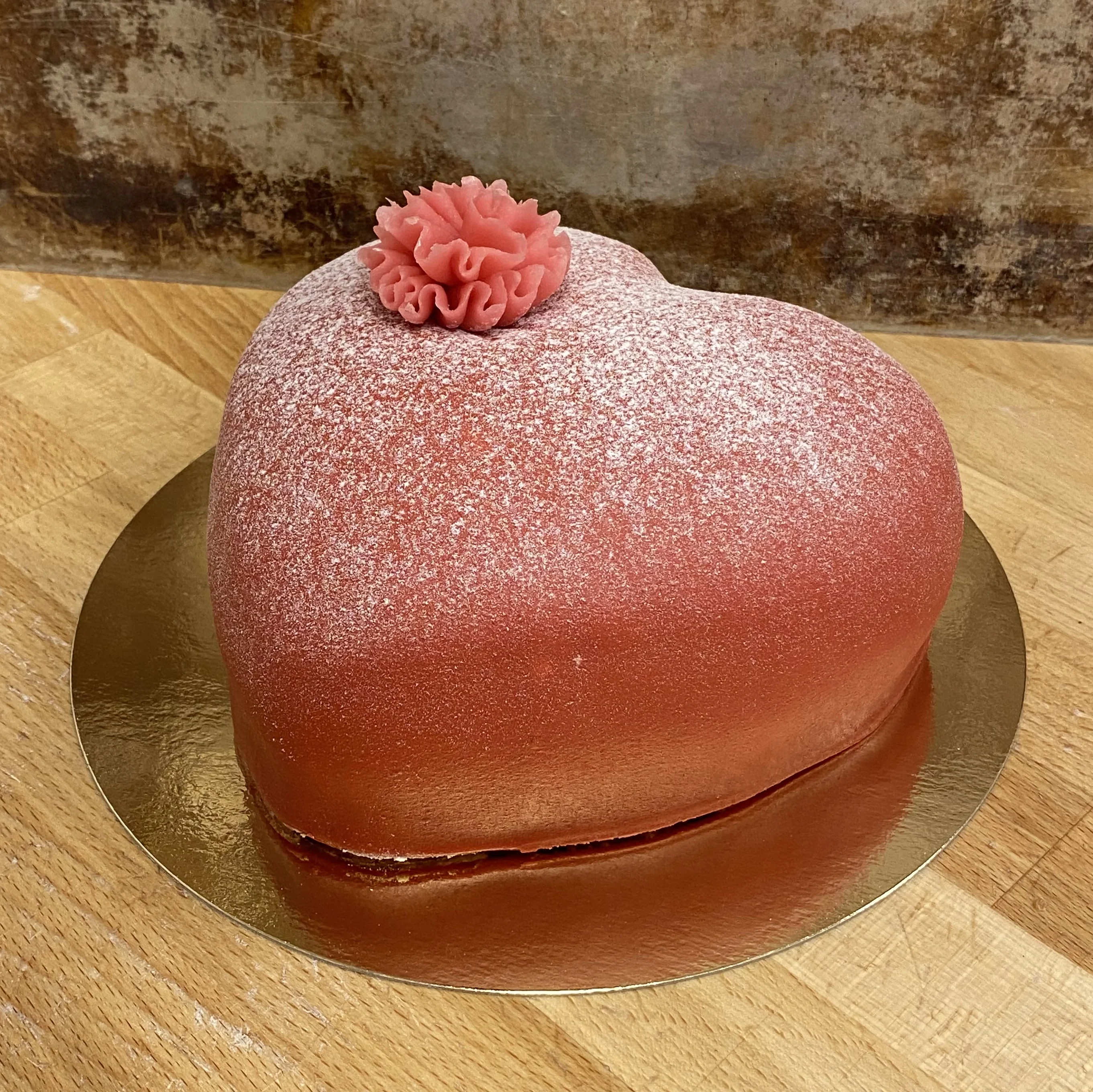 En röd prinsesstårta, formad som ett hjärta och dekorerad med en rosa nejlika.