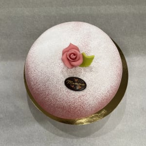 Opera tårta med hallonsylt, vaniljkräm och lättvispad grädde. Täcks med rosa marsipan och chokladsigill med text Mamma.