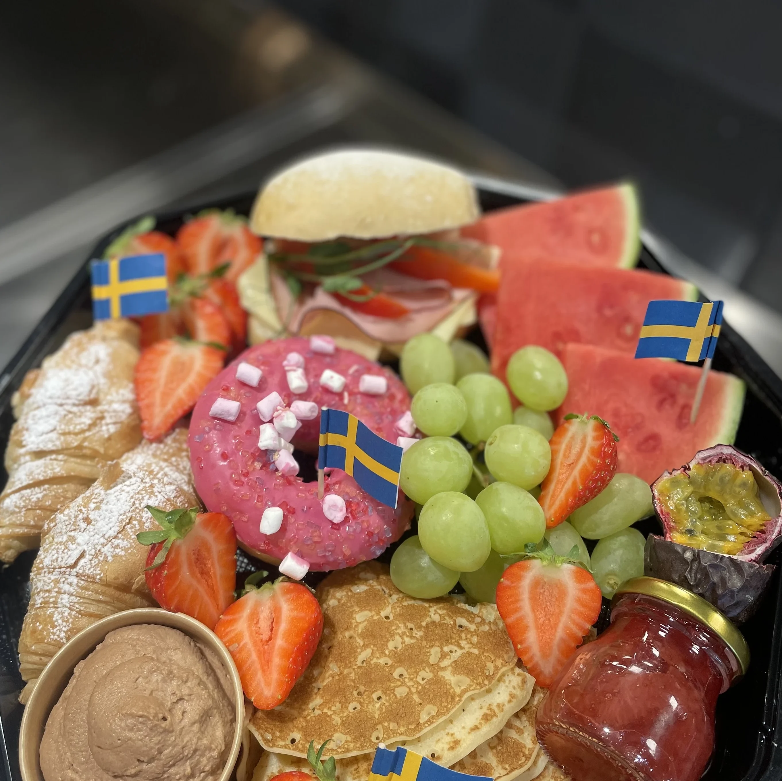 Brunchbricka, innehåller pannkaka, fralla, frukt, croissant, sylt, nutellagrädde, donut.