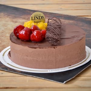 Rund chokladtårta gjord av mousse. Dekorerad med choklad, röda jordgubbar och gul frukt på ena delen av tårtan.