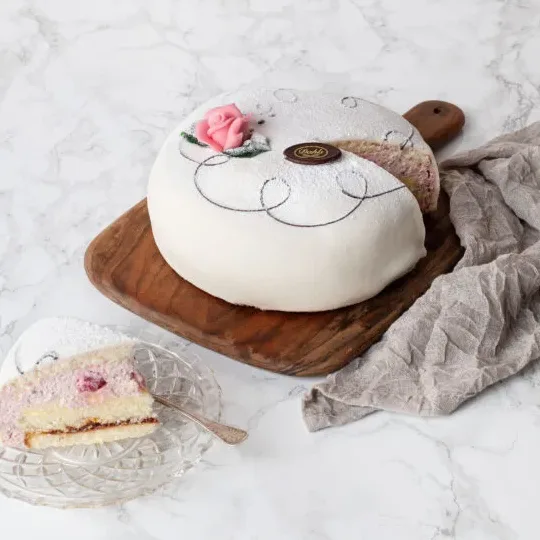 Oskuldsfull och vacker i vit marsipan. Mellan tre hembakta sockerkaksbottnar samsas vår egna vaniljkräm och fluffig grädde och rikligt med hallon. Vår rekommendation