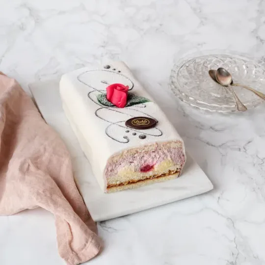 Oskuldsfull och vacker i vit marsipan. Mellan tre hembakta sockerkaksbottnar samsas vår egna vaniljkräm och fluffig grädde och rikligt med hallon.