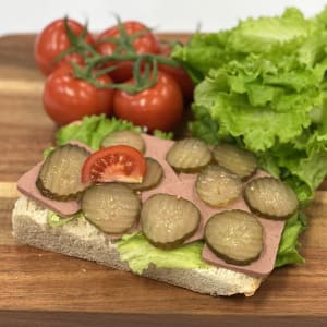 Nybakat bröd med leverpastej, smörgåsgurka, sallad, tomat och gurka.