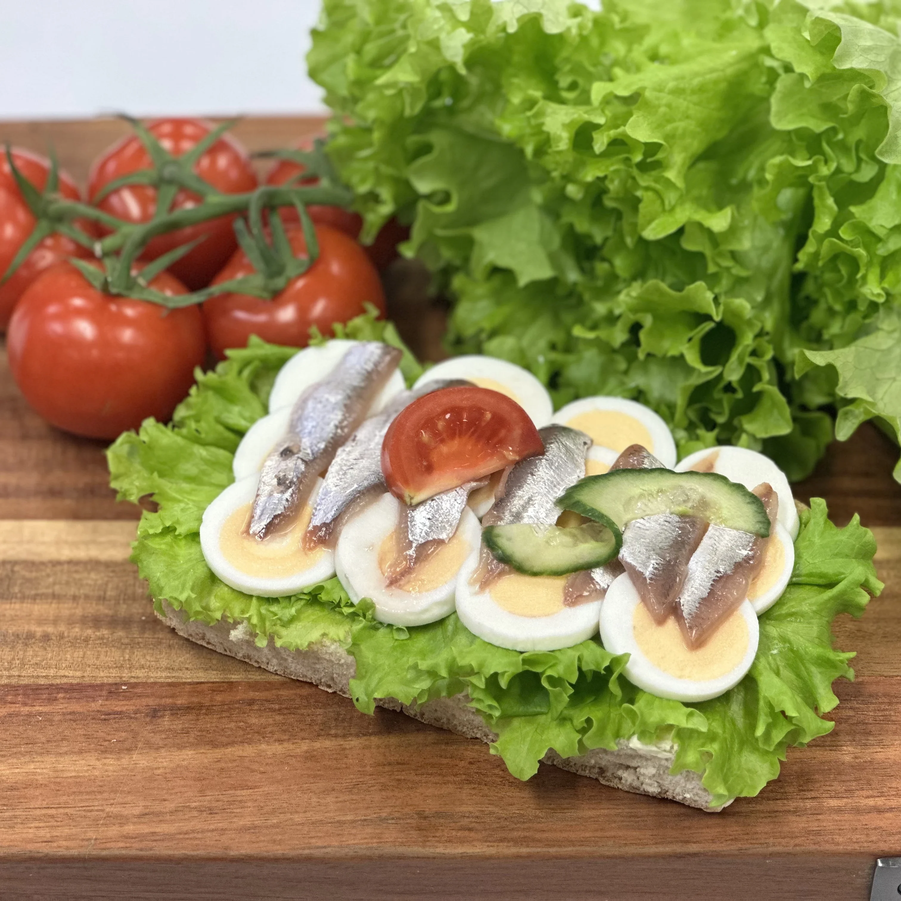 Nybakat bröd med kokt ägg, anjovis, sallad, tomat och gurka.