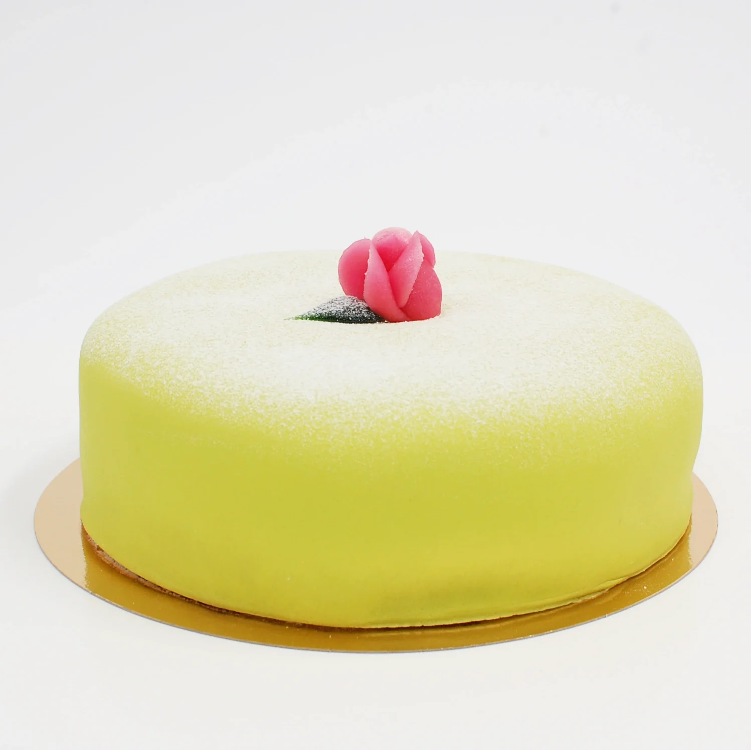 En grön prinsesstårta är täckt med ett lager av grön marsipan och dekorerad med en rosa marsipanros och florsocker på toppen.