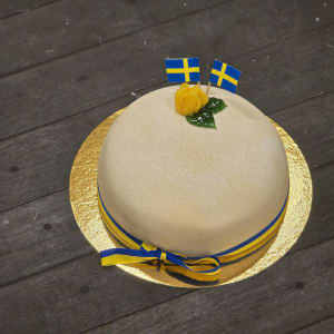 En vit marsipantårta med gul ros, Sverigeflaggor och band.