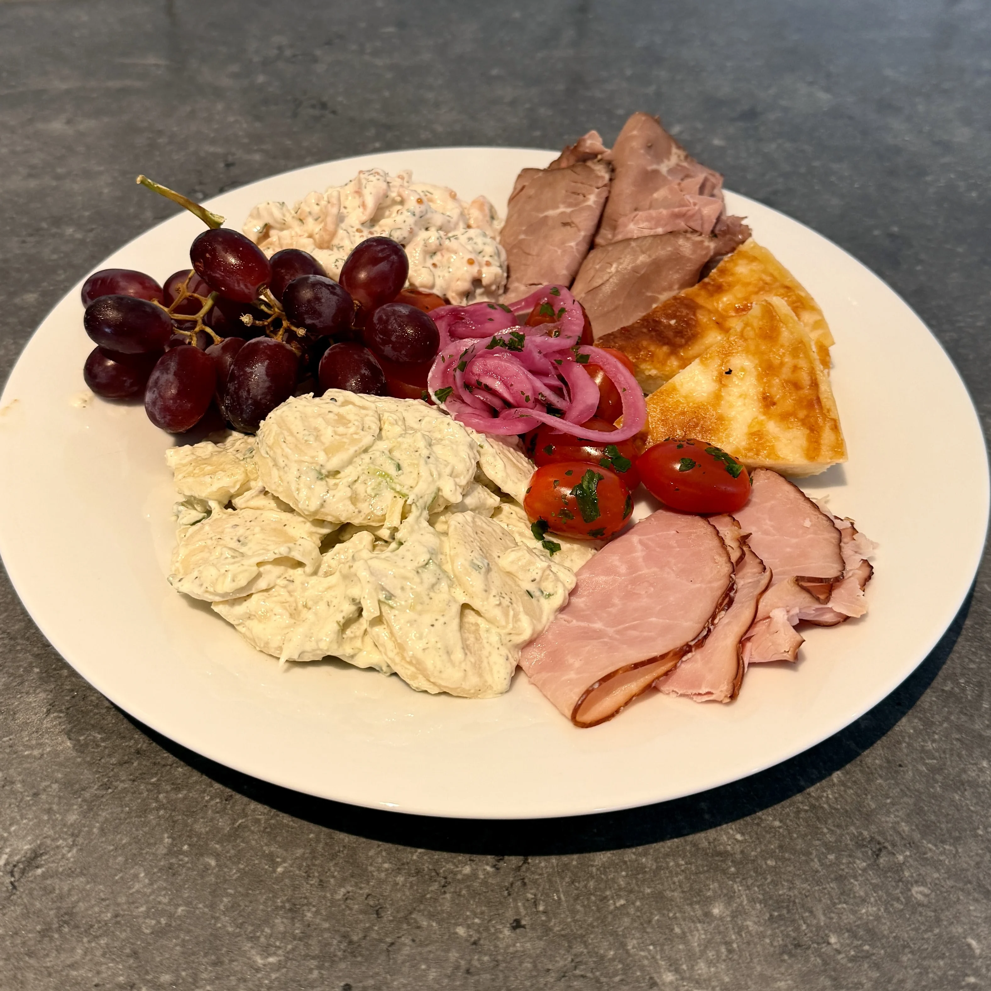 Tallrik med skinka, vindruvor, paj, potatissallad, picklad rödlök, tomater