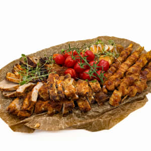 Ett grillmix fat med fem olika sorters kött och lite tomater för dekoration.