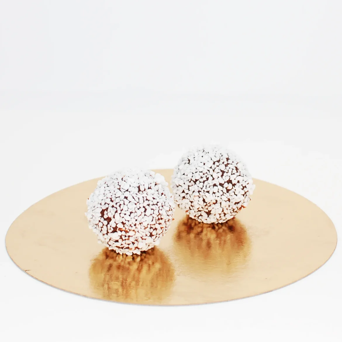 Två stycken chokladbollar täcka med pärlsocker ståendes på en rund guldbricka