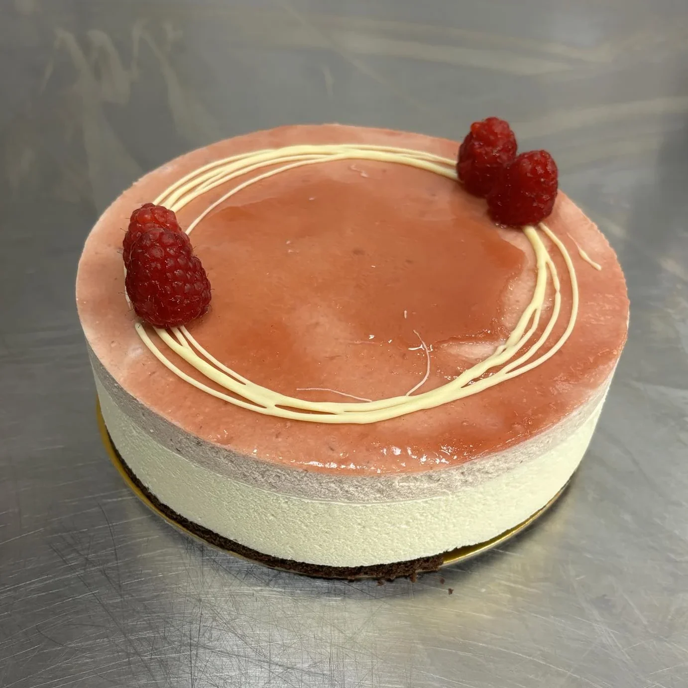 Mjuk chokladtårtbotten med lager av hallonmousse, krämig vit chokladmousse och hallonkompott. Toppad med hallonglaze, vitchoklad och färska hallon.