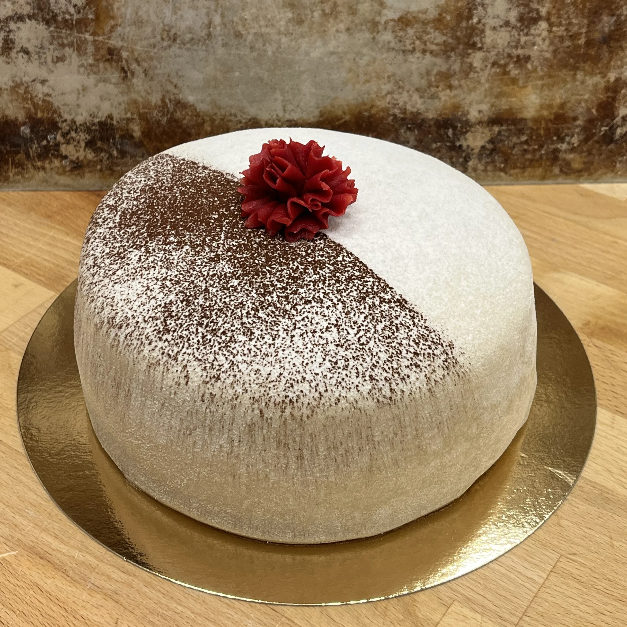 Innehåll chokladsockerkaksbottnar, vaniljkräm och chokladgrädde. Dekorerad med vit marsipan och kakao samt en röd nejlika.