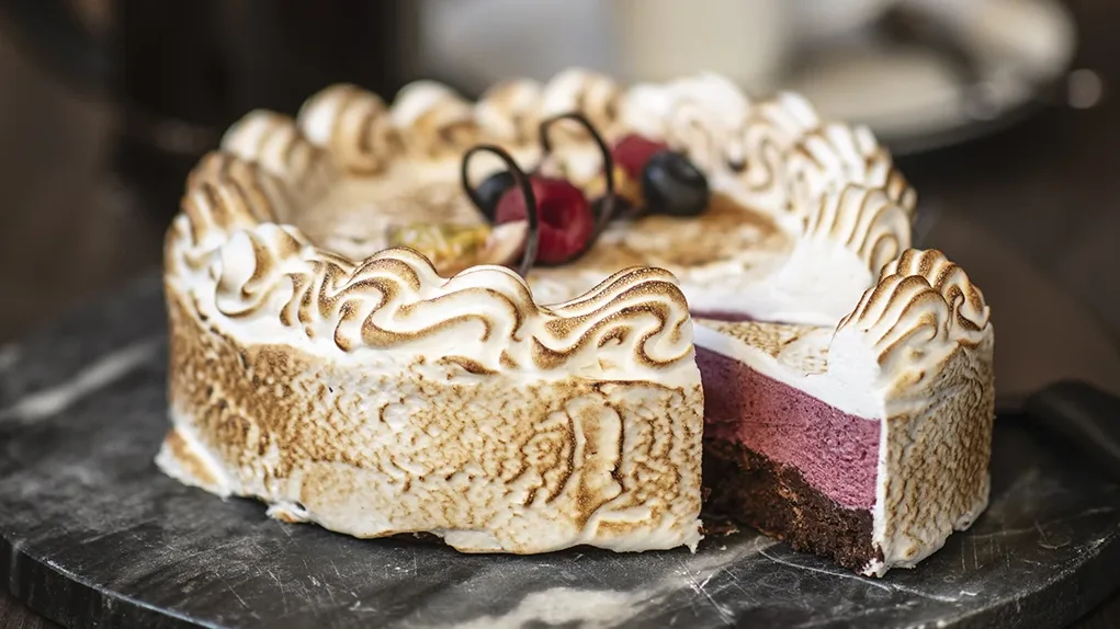 Vacker ljuvlig tårta med chokladbotten svartvinbärsmousse och italiensk maräng