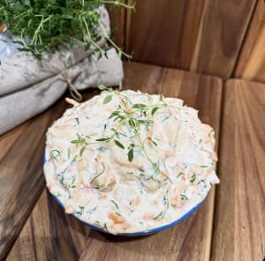 En skål fylld med skagenröra toppad med en kvist timjan på ett fat