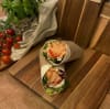 på bilden är det en laxwrap gjord på tortillabröd. fylld med varmrökt lax, provensalsk sallad, fetaostcremé, tomat.