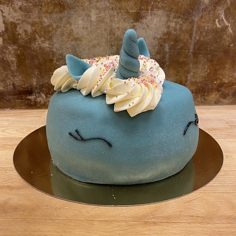 En blå tårta med grädde som man, öron och horn i marsipan. Dekorerade ögon på sidan av tårtan.