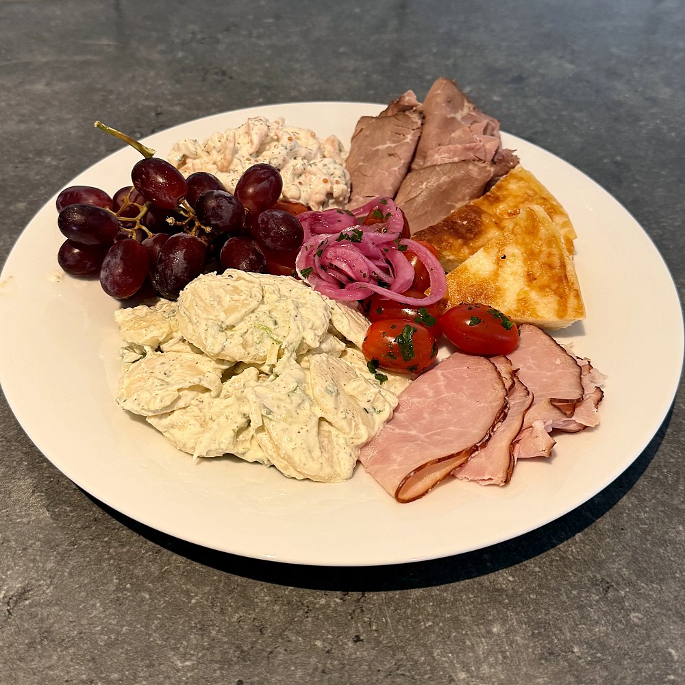 Tallrik med skinka, vindruvor, paj, potatissallad, picklad rödlök, tomater