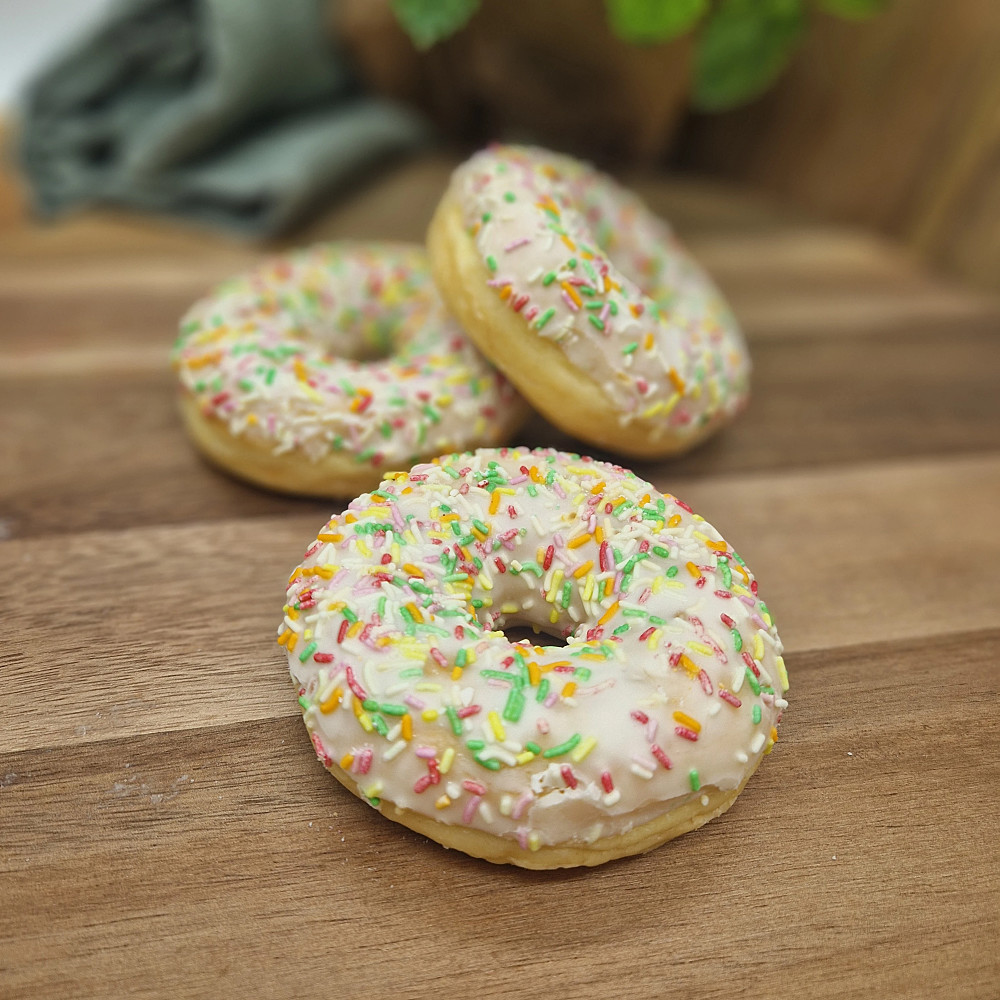 Donut frutti med bärfyllning och strössel på träbricka. Fika på fikabord.