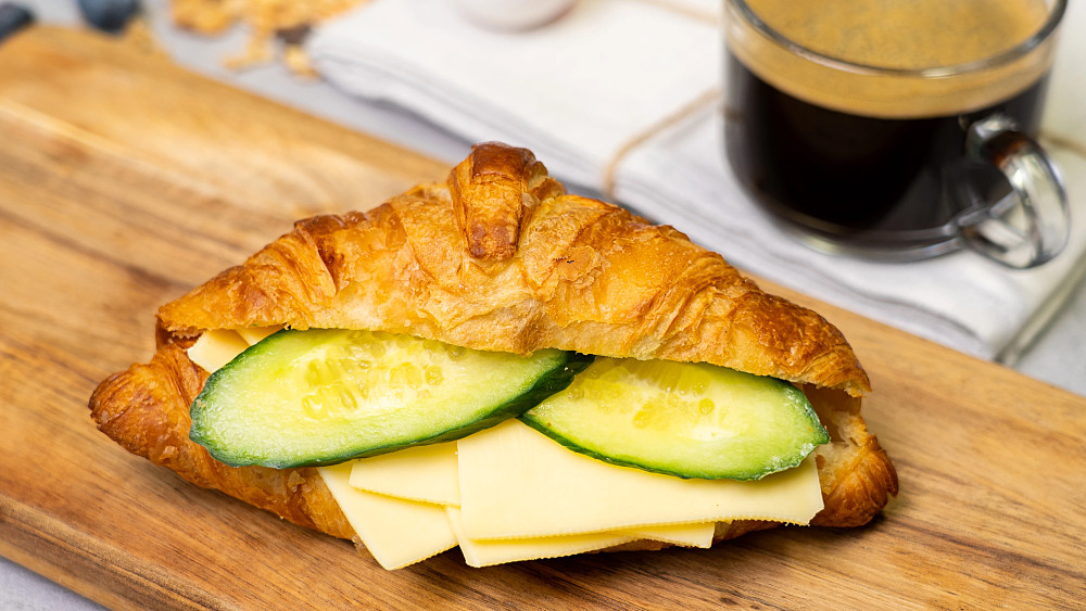 En nybakad croissant med ost och gurka. Bild av en frukostmacka med en kopp kaffe.