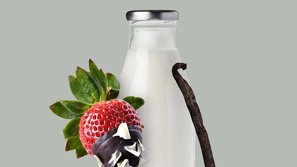 En kanna med mjölk. En chokladdoppad jordgubbe spetsad på en gaffel. En vaniljstång lutar mot mjölkkannan