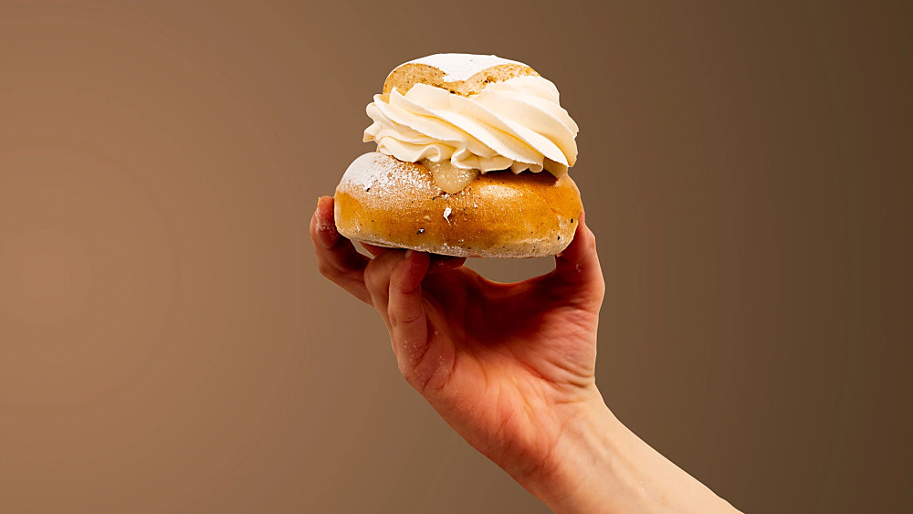 Två semlor som hålls mot en brun bakgrund