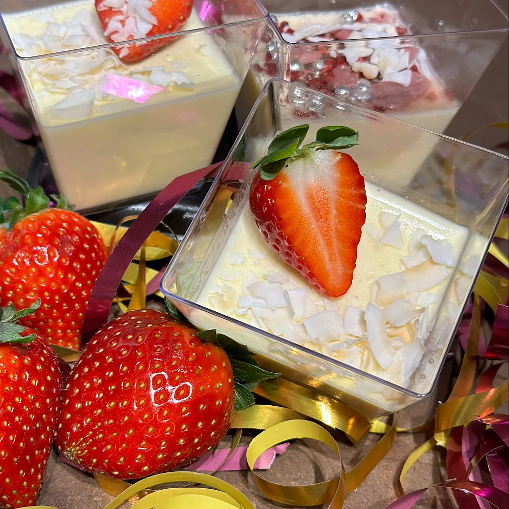 Vaniljpannacotta i en fyrkantig dessertskål gjord av plast, toppad med blåbär och hallon.