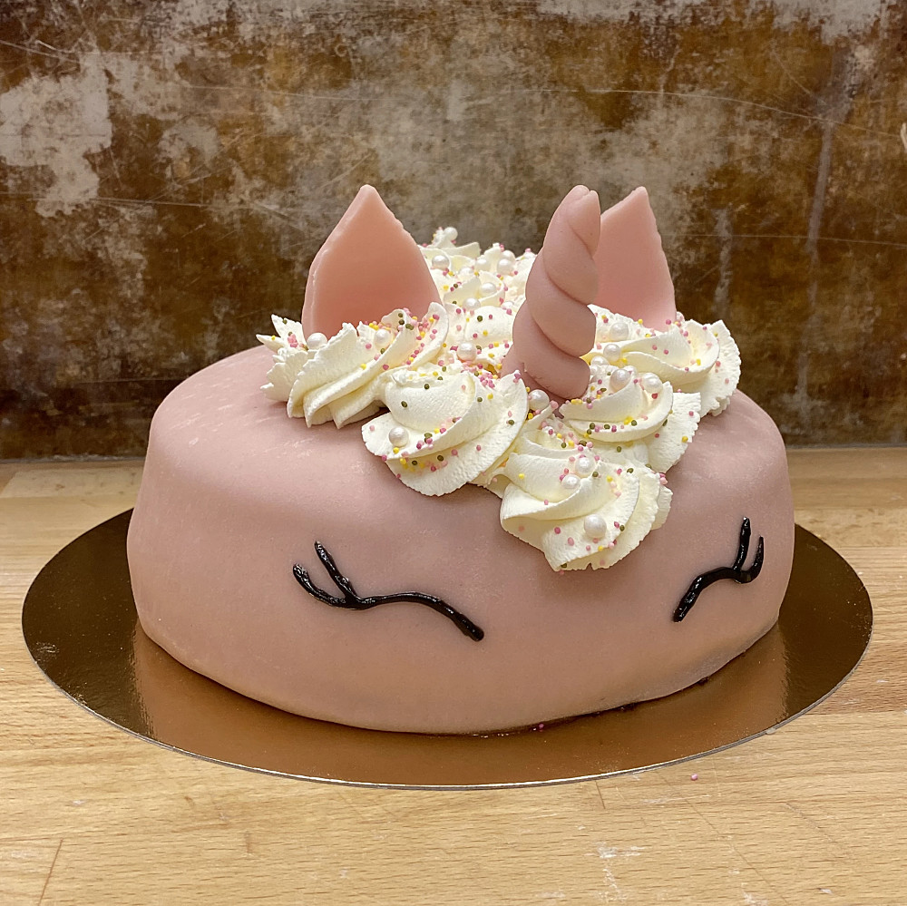 En rosa tårta med grädde som man, öron och horn i marsipan. Dekorerade ögon på sidan av tårtan.