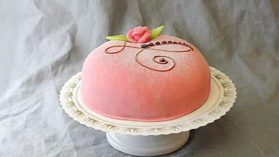 En klassiskt god tårta på sockerkaksbotten med fyllning av vaniljkräm och grädde samt ett lager ljuvlig hallonsylt. Täckt med rosa marsipan.