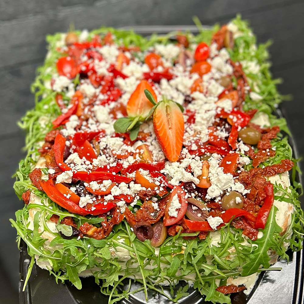 Vegetarisk smörgåstårta med fetaostkräm och kräm på soltorkade tomater, garnerad med ruccola och grönsaker