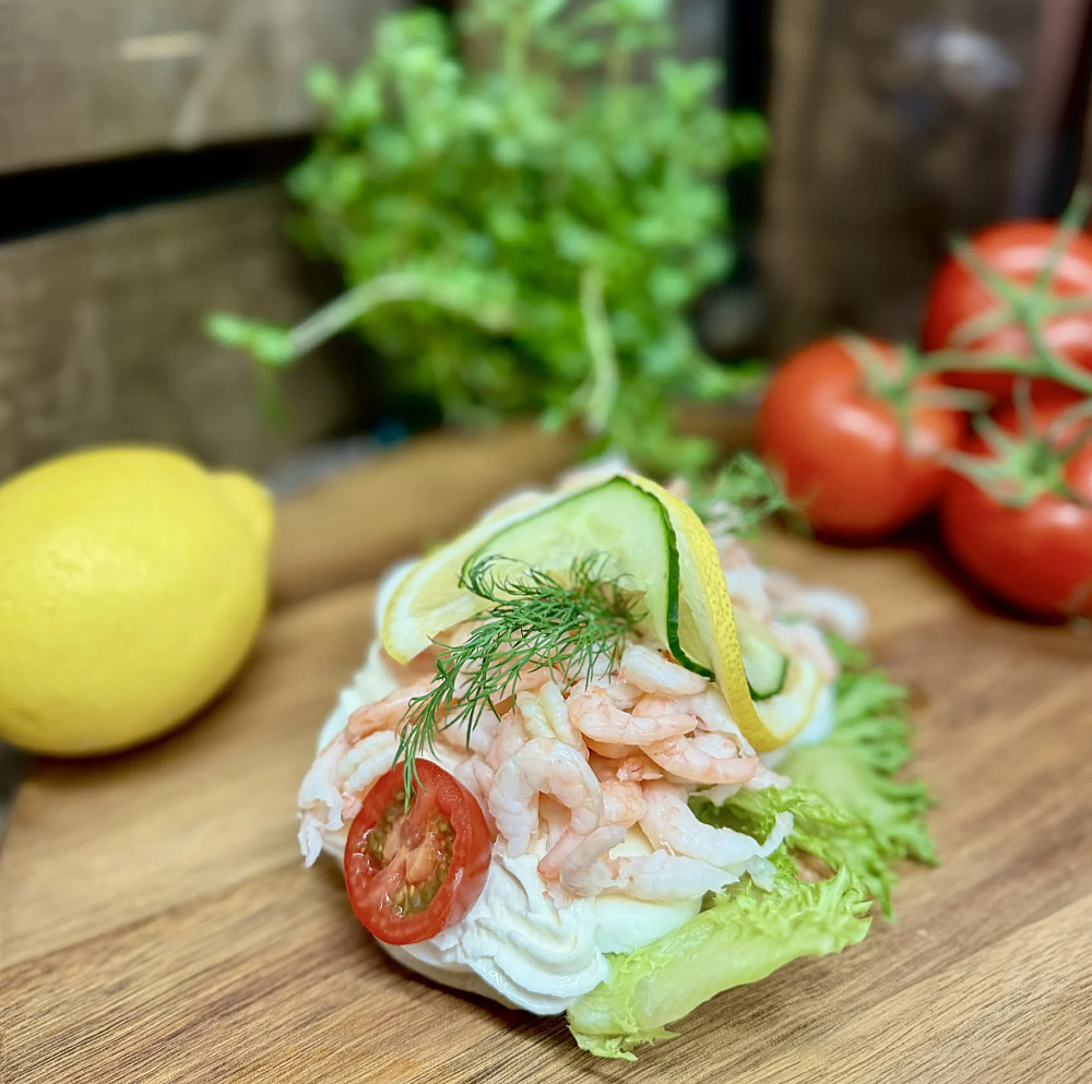 En räksmörgås dekorerad med sallad, tomat, gurka, citron och dill